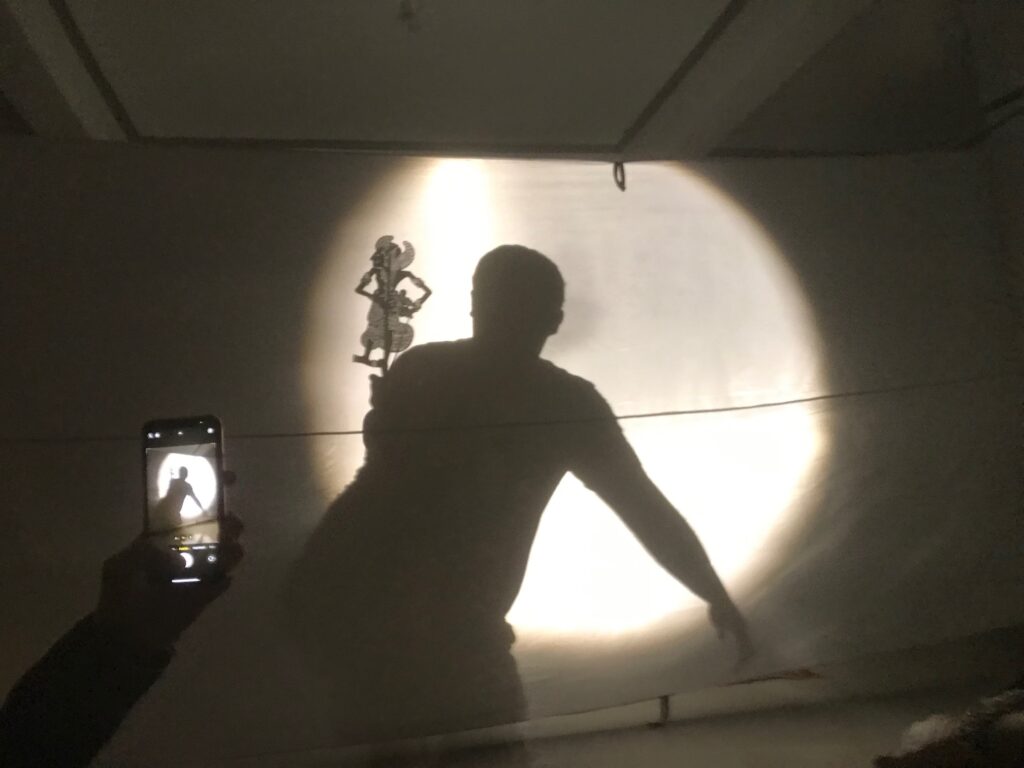 Shadow caster behind the projection screen with wayang kulit figure. (Photo: I Made Sidia)