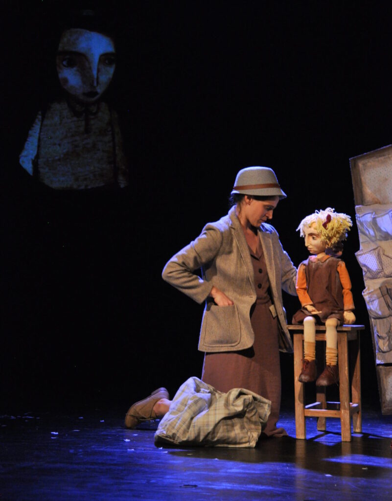 Hava the Adult as her mother, changing the identity of Hava the Puppet Child, while Hava the Puppet Animation observes. (Photo: Alon Piat)