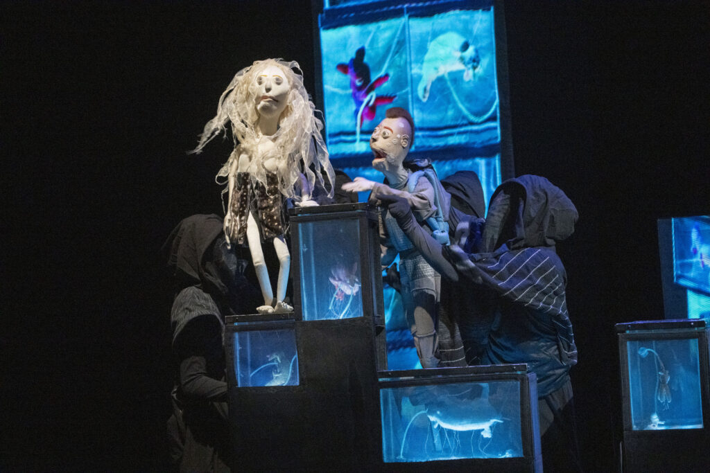 Figure 3. Aurelia and Bug converse in front of Aurelia’s tanks in The Immortal Jellyfish Girl. Wakka Wakka ensemble. (Photo: Richard Termine)