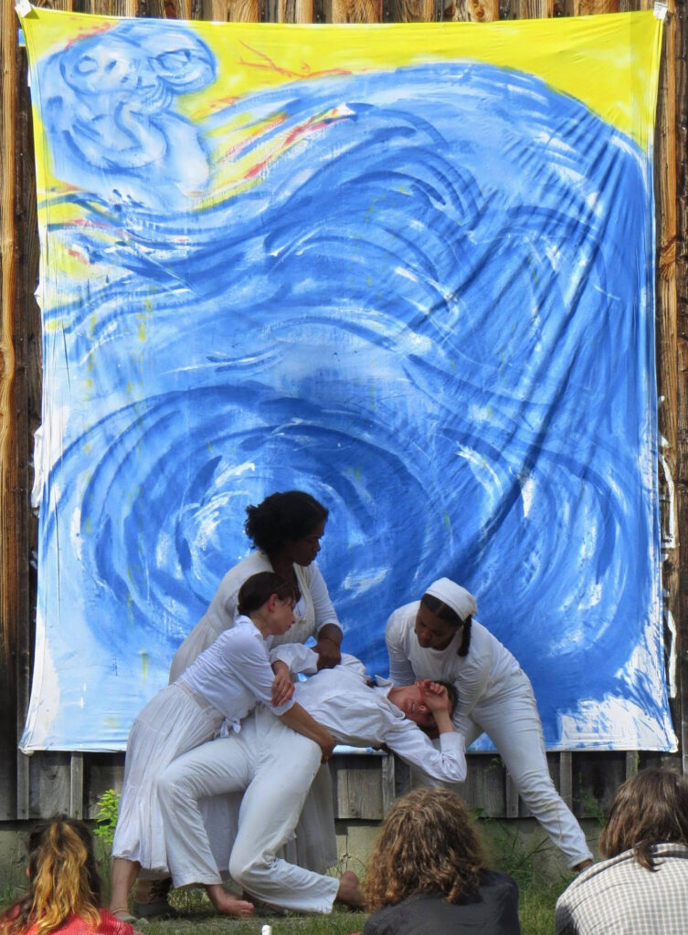 Figure 1. Esteli Kitchen, Torri-Lynn Francis, Maura Gahan, and Savannah Omani Wade in a scene from the summer 2021 outdoor performance of Bread and Puppet Theater’s The Persians. The bedsheet painting is #4 of Peter Schumann’s “Persians” series. (Photo: Courtesy of Bread and Puppet Theater)