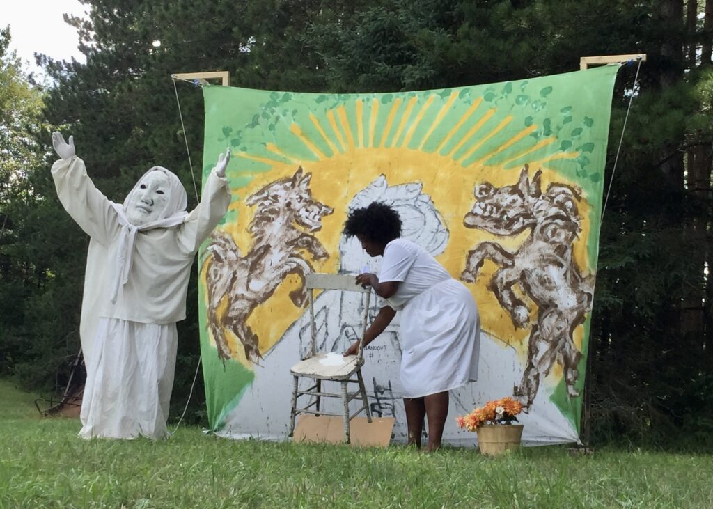 Figure 4. Joshua Krugman (in mask) and Torri-Lynn Francis performing their sideshow Palestine as part of the 2021 Domestic Resurrection Circus and Pageant in Glover, Vermont, with bedsheet #25 of the “Handout” series. (Photo: John Bell)